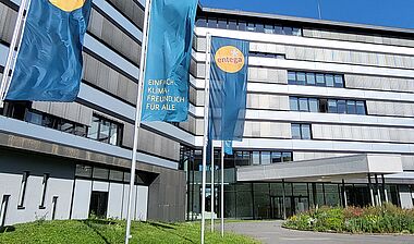 Modernes Bürogebäude der ENTEGA mit Fahnenmasten, Grünflächen und einem blauen Himmel.